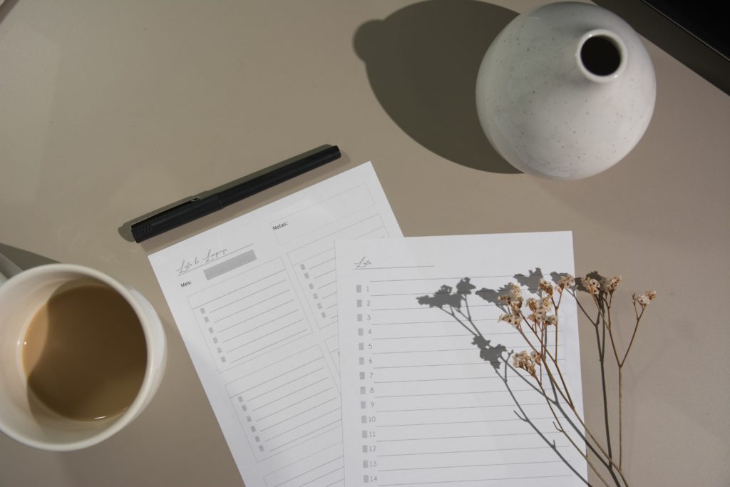 Checklist with pen, cup of coffe, flowers, and a vase sitting on a tabletop
