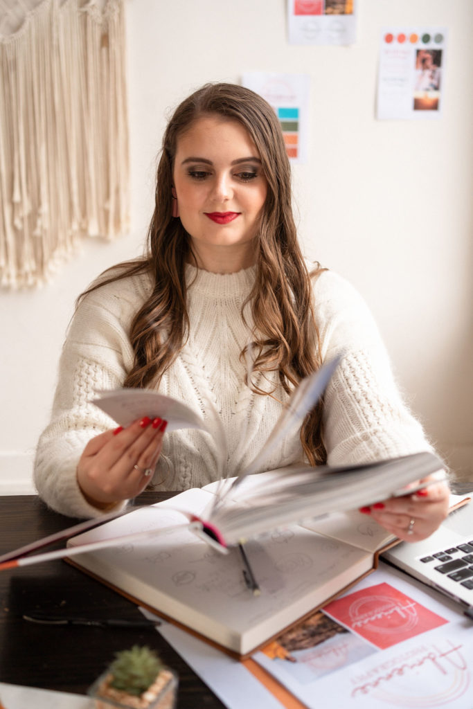 Emily Foster wearing a white sweater and flipping through a book to identify her ideal client.