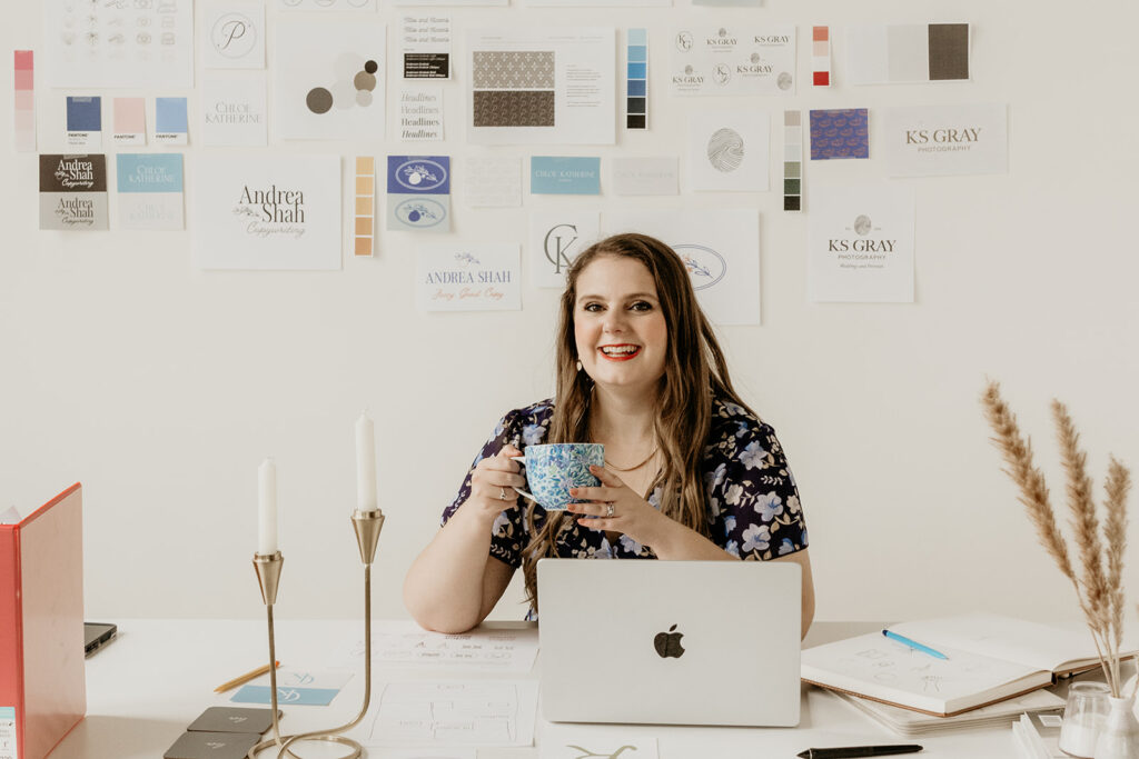 Emily Foster, owner of Emily Foster creative, and brand and website designer, sitting at a desk with a laptop and cup of tea