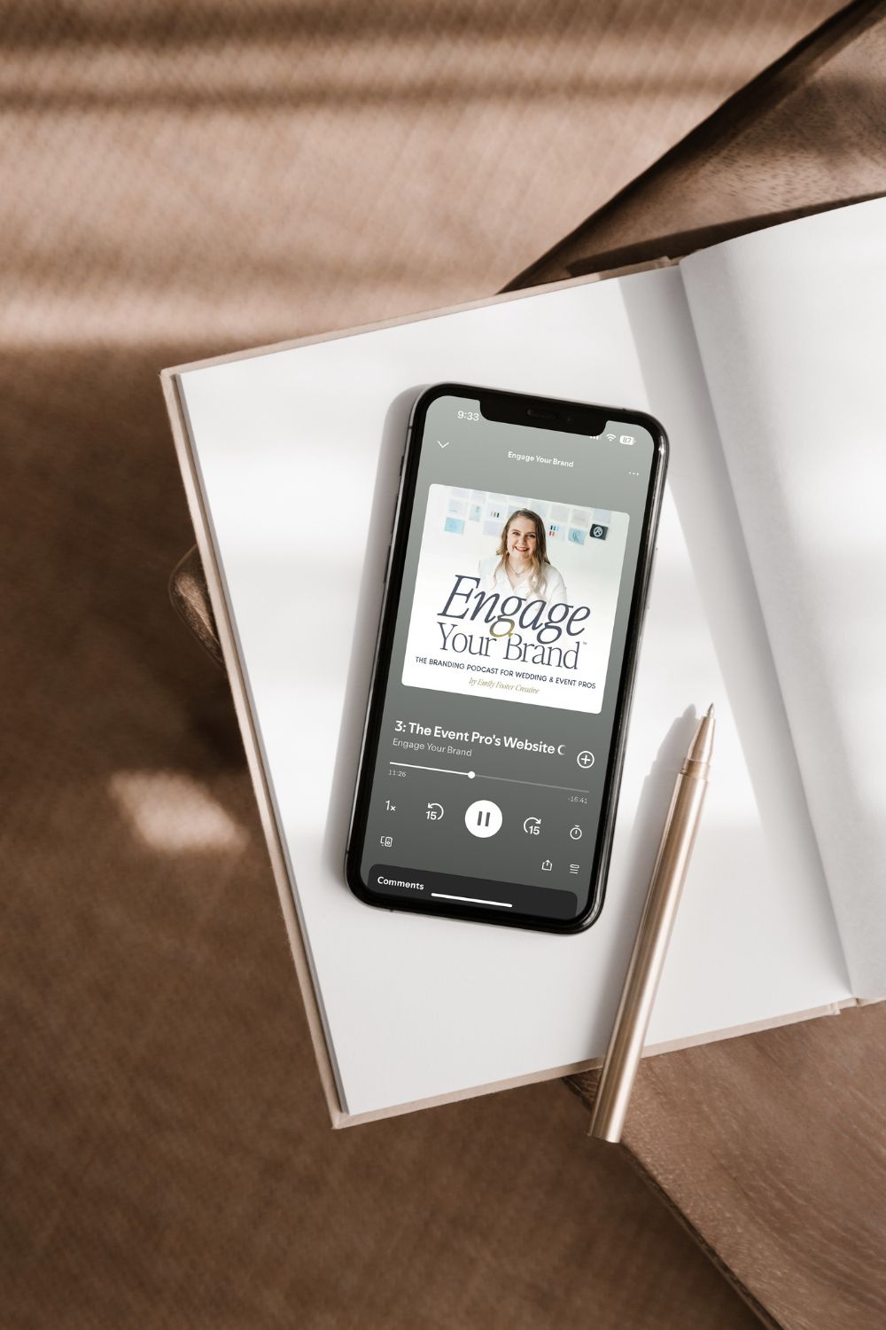Engage Your Brand podcast playing on a phone sitting on an empty notebook