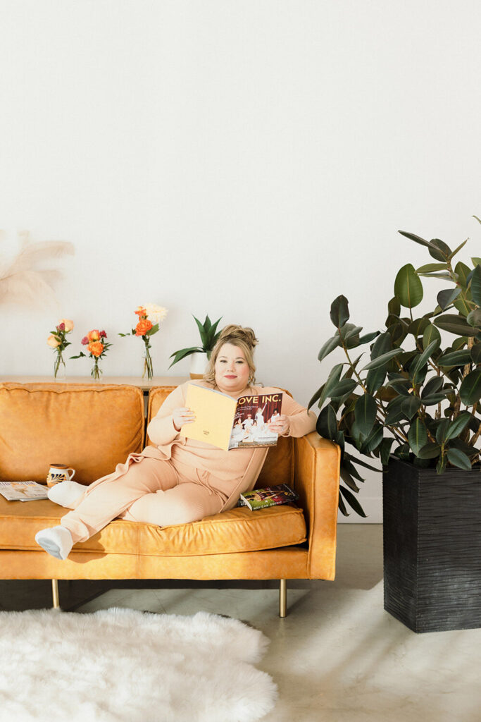 Cinthia, sitting down on an orange couch holding a magazine