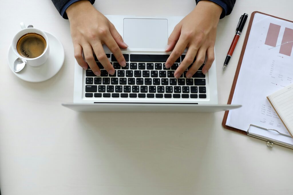 Someone's hand working on a laptop with things beside it