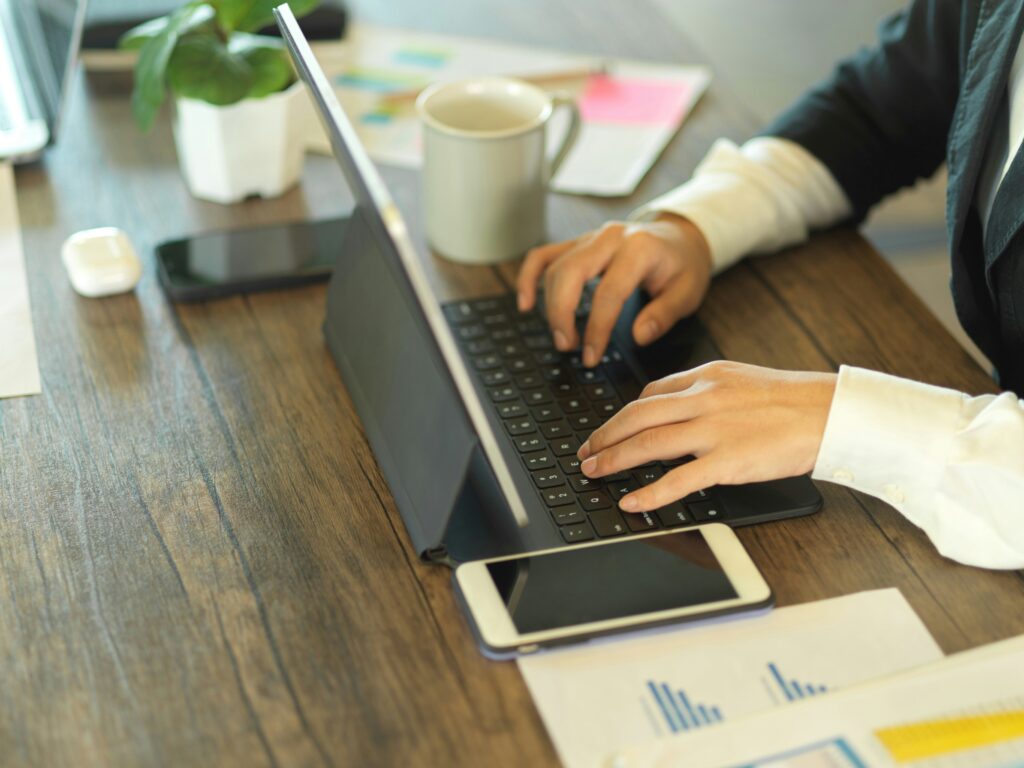 Hands working on a laptop with mug, phone and papers on the table