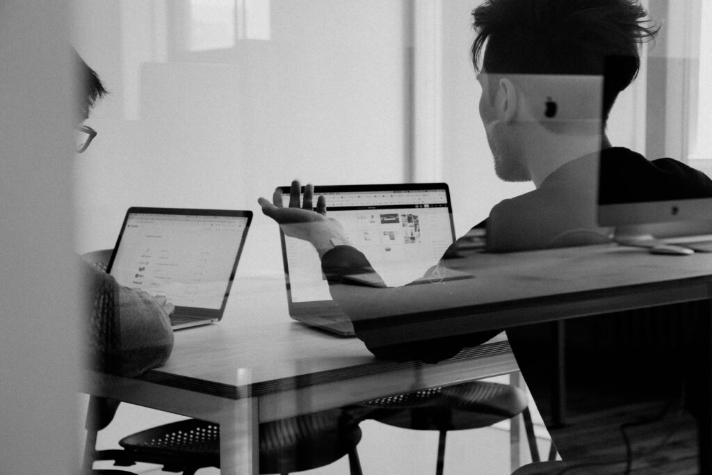 Black and white photo of two people discussing facing their laptops