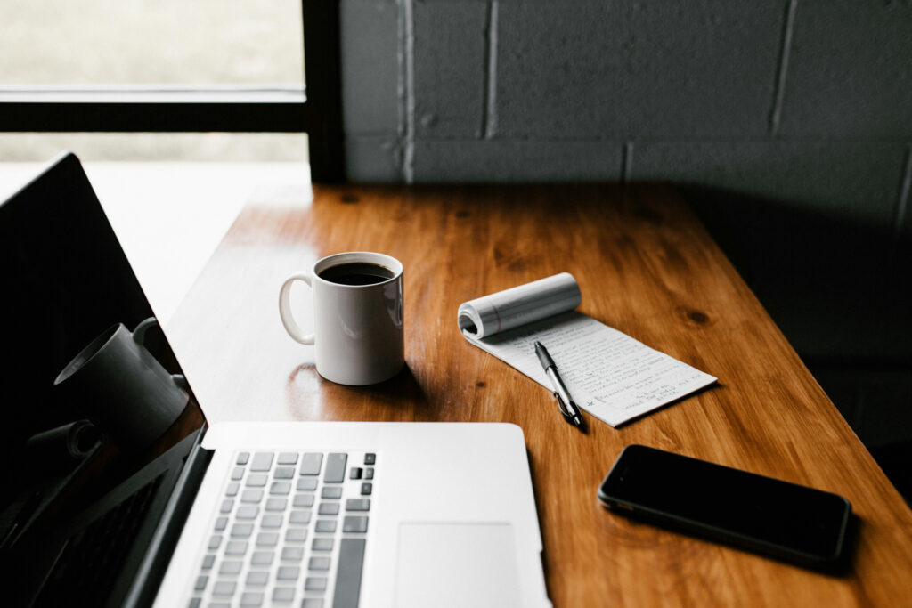 Laptop, coffee, and notebook on wooden desk workspace