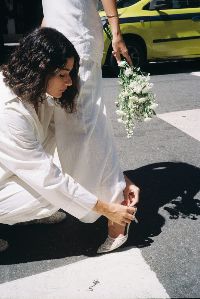 Woman adjusting bride's shoes while holding bouquet outdoors