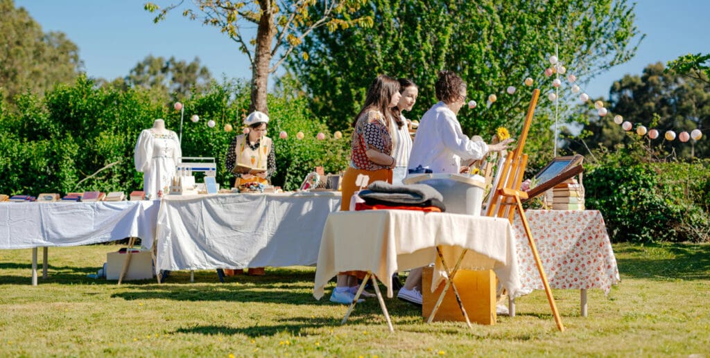 Outdoor vendor market with creatives setting up tables on a sunny lawn