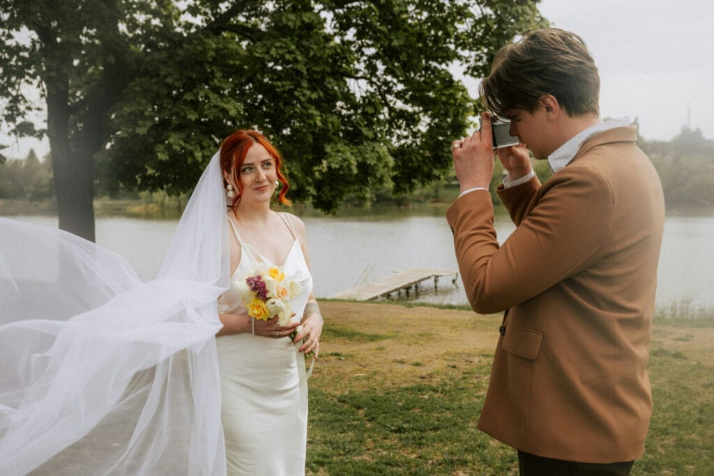 Groom taking a photo of the bride near the water on their wedding day