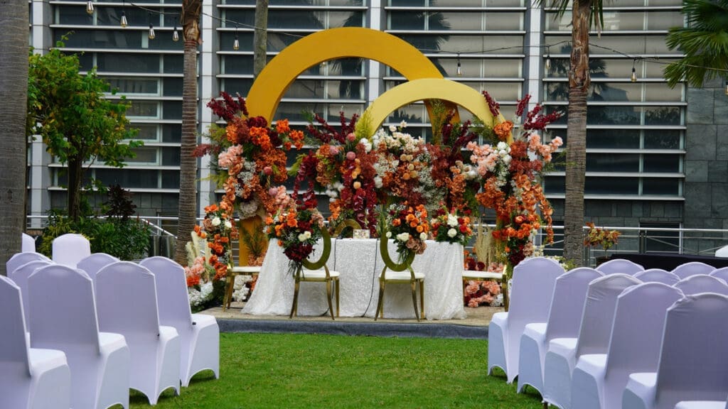 Outdoor wedding ceremony setup with colorful floral arch and white chairs