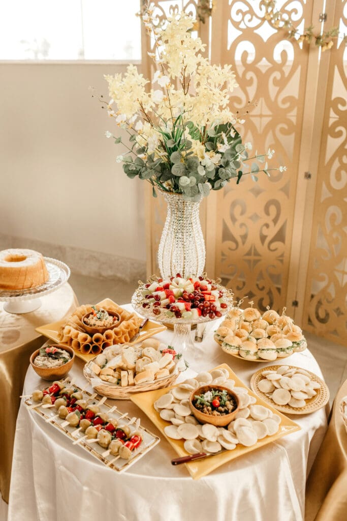 Catered appetizer table with small bites, fruit, and floral arrangements