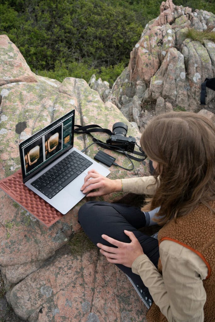 Photographer editing photos on a laptop outdoors on rocky terrain