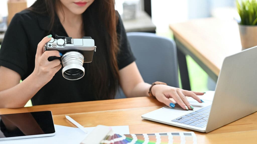 Photographer holding a camera while working on a laptop