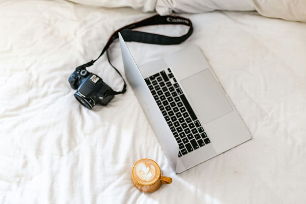 Camera, laptop, and coffee arranged on a bed