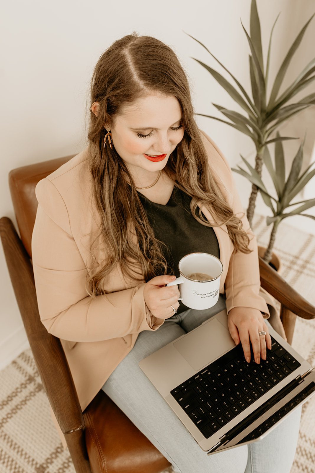 Woman in professional attire holding a coffee cup while sitting at a computer reviewing website copy