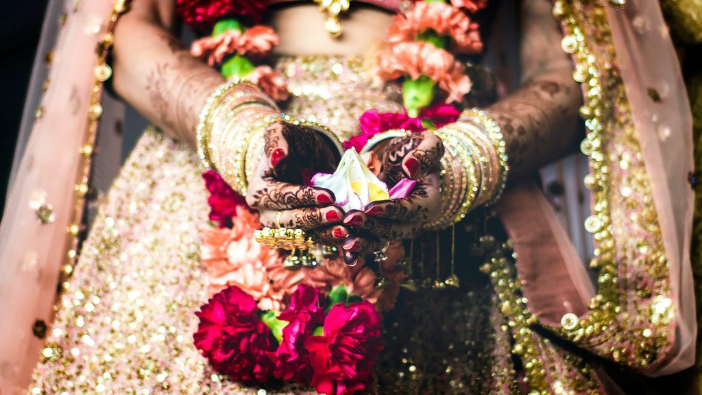 Bride holding flowers with henna designs and gold jewelry.