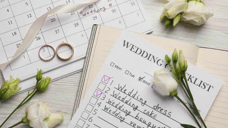 Wedding planning checklist with rings, calendar, and white flowers.