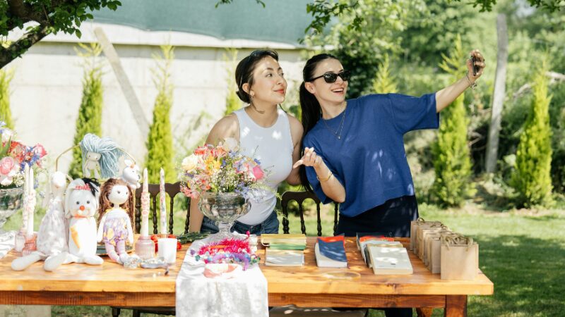 Two women taking a selfie at an outdoor vendor table